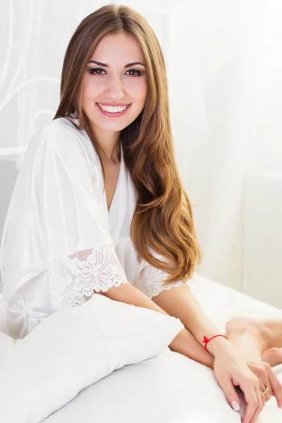 Sonriente chica está sentado en la cama blanca — Foto de Stock