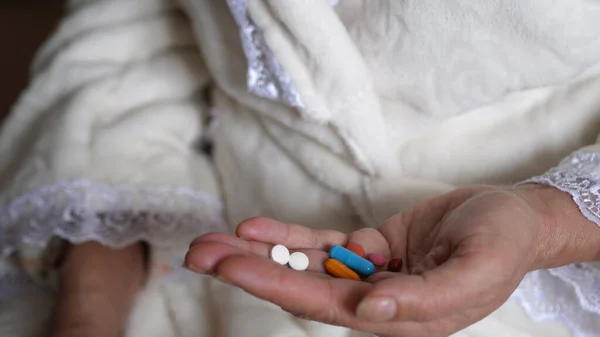 Senior adult woman taking medicine in pills. Pours out of bottle on palm hand capsules of vitamin analgesic antibiotics antiviral. Old people senior takes medicine and health care. Close up view