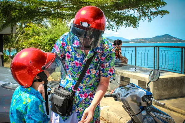 father and son wearing helmets are going to go on a motorbike in Koh Samui