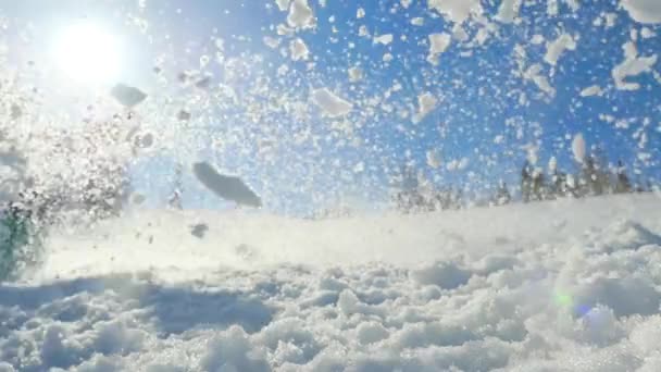 junger Mann beim Snowboarden auf Bergen in der Sonne und klopfte den Schnee in die Kamera. Zeitlupenaufnahmen