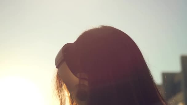 Lassított fiatal nő hallgat zenét fejhallgató a város naplemente. Flörtölés és küldése csók a kamerába