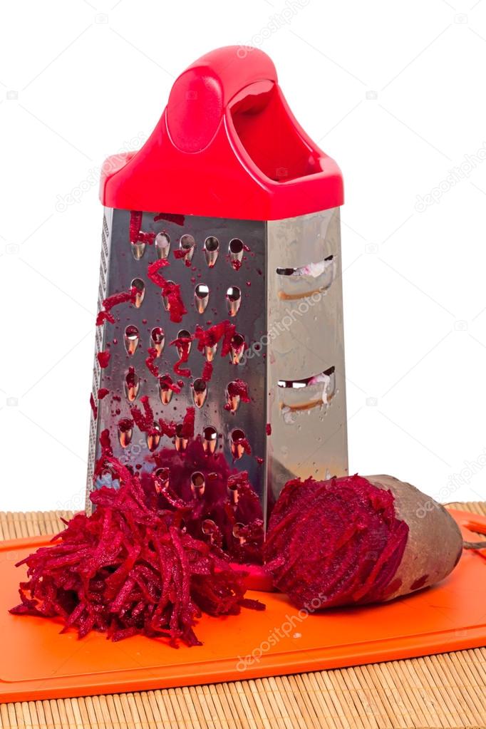 Pile of grated red beets and grater on white