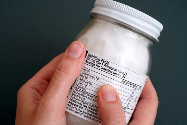 Coconut oil jar with nutrition facts in woman hands — Stock Photo, Image