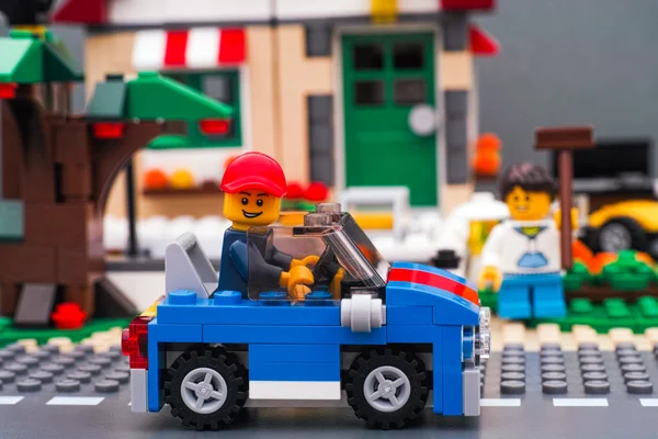 Lego man sitting in blue car on road in front of house — Stock Photo, Image