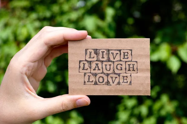 Woman hand holding cardboard card with words Live Laugh Love — Stock Photo, Image