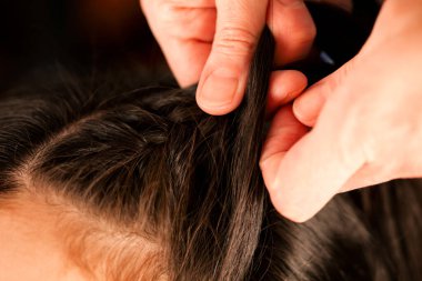 Kadın elleri esmer kızları uzun saçlarıyla örüyor. Yakın plan.