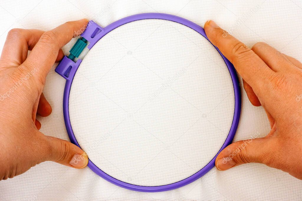 Purple plastic embroidery hoop with white cross stitch fabric in woman hands
