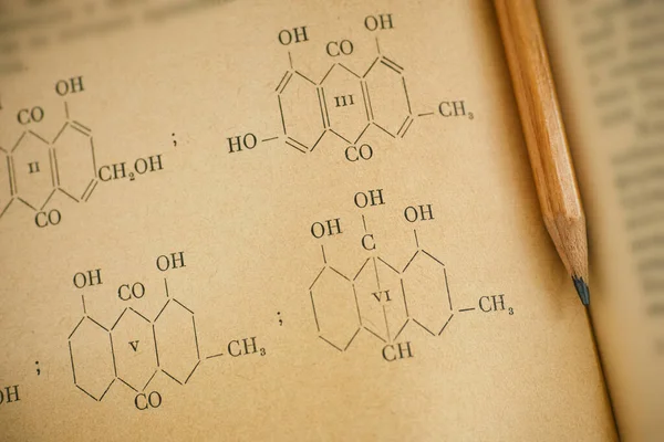 Open page of old chemistry book with chemical formulas and pencil. Close-up