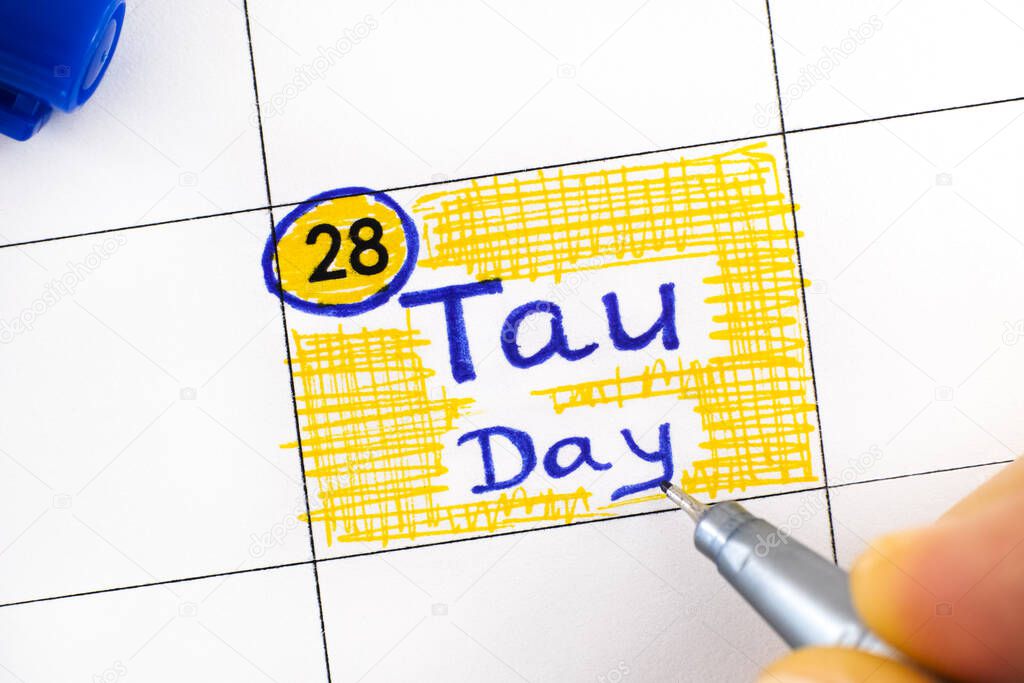 Woman fingers with pen writing reminder Tau Day in calendar. June 28.