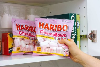 Tambov, Russian Federation - January 25, 2021 Woman hand taking Haribo Chamallows package out of cupboard shelf.