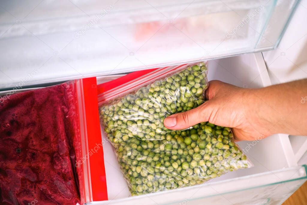 Woman hand taking homemade packing of green peas out of freezer. Close-up