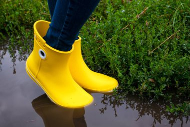 Yağmurdan sonra su birikintisinde sarı çizmeli bir kadın. Yakın plan.