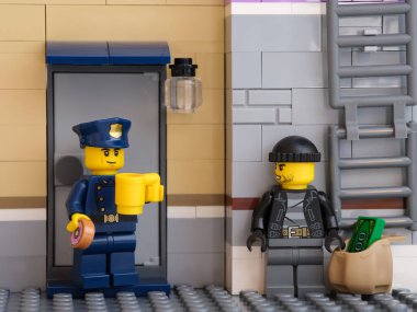 Tambov, Rusya Federasyonu - 05 Temmuz 2021 Lego polisi kahve içip çörek yerken soyguncu köşede bir çanta dolusu parayla saklanıyor.