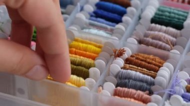 Bir kadın eli, sarı turuncu nakış ipliğini ayıran kutudan seçer ve alır.