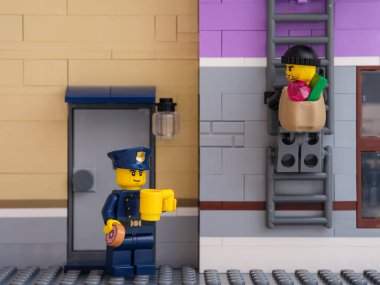 Tambov, Rusya Federasyonu - 5 Temmuz 2021 Bir Lego polisi kahve içip çörek yerken soyguncu bir çanta dolusu para ve mücevherle kaçmak için merdivene tırmanıyor.