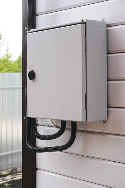 An electrical panel with an electric wires in it on a wall outside the house.