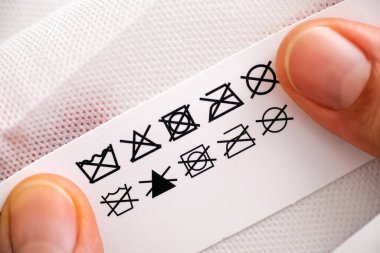 Kadının elleri etiketi polyester şeyin temizlik talimatlarıyla tutuyor - yıkama; çamaşır suyu dökme; kurulama; düzleştirmeyin; ütülemeyin; kuru temizleme.