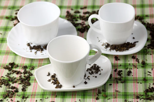 Trois tasses blanches vides et soucoupes avec feuilles de thé vert renversées — Photo