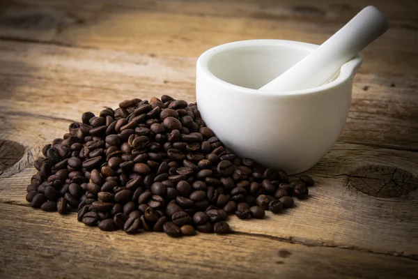 Grãos de café em fundo de madeira e argamassa branca Imagem De Stock