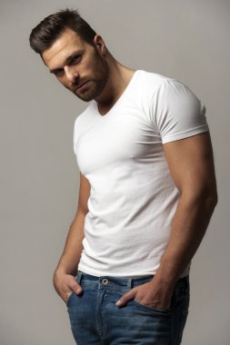 Handsome young man in white t shirt and jeans on gray background
