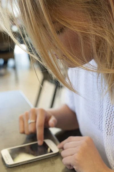 Menina loira bonita olhando e digitando no smartphone no café — Fotografia de Stock