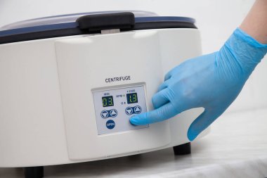 Mavi eldivenli bir el santrifüj düğmesine basıyor..