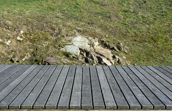 Tavole di legno, erba e rocce sullo sfondo — Foto Stock