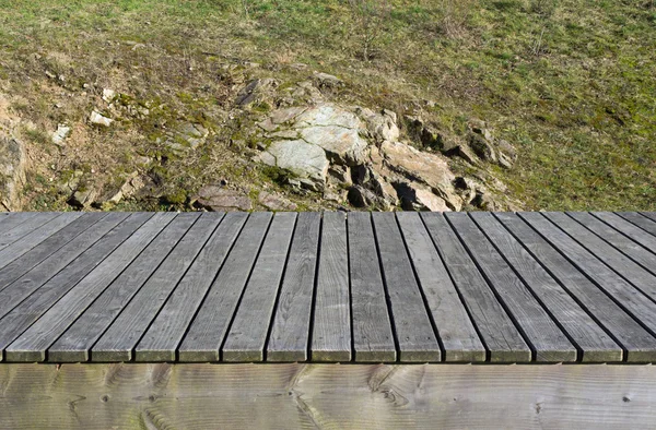 Tavole di legno, erba e rocce sullo sfondo — Foto Stock