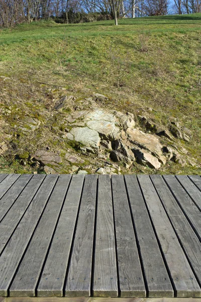 Houten planken, gras en rotsen op de achtergrond — Stockfoto