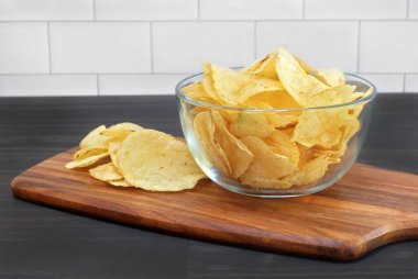 Potato chips in a glass bowl on a table in a close up macro view.  Bowl sitting on cutting board.