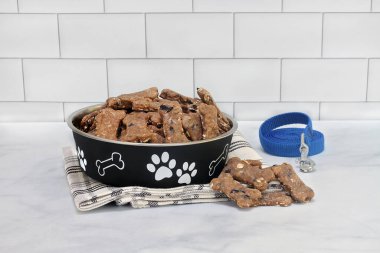 Homemade, healthy blueberry dog cookies on a counter and in a dog bowl with a leash on the side. clipart