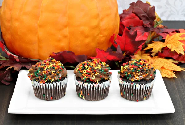 Tres cupcakes de chocolate en fila frente a las decoraciones de otoño —  Fotos de Stock