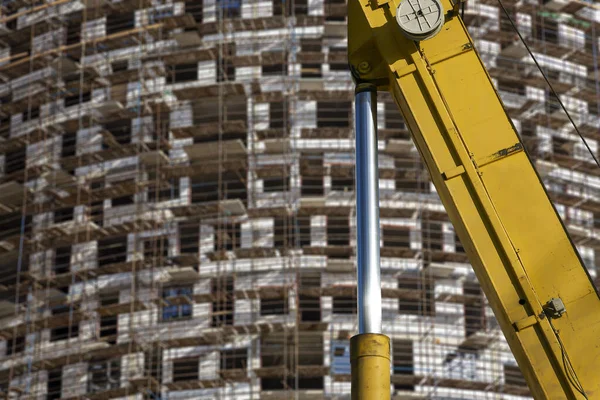 Part of a construction machine (excavator or crane) with multi-storey building under construction with scaffolding (new residential complex) on the background, Moscow, Russia