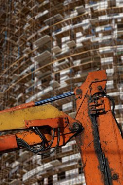 İnşaat makinesinin bir parçası (kazıcı veya vinç) arka planda iskele (yeni iskan kompleksi) bulunan çok katlı bina, Moskova, Rusya