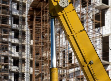 İnşaat makinesinin bir parçası (kazıcı veya vinç) arka planda iskele (yeni iskan kompleksi) bulunan çok katlı bina, Moskova, Rusya