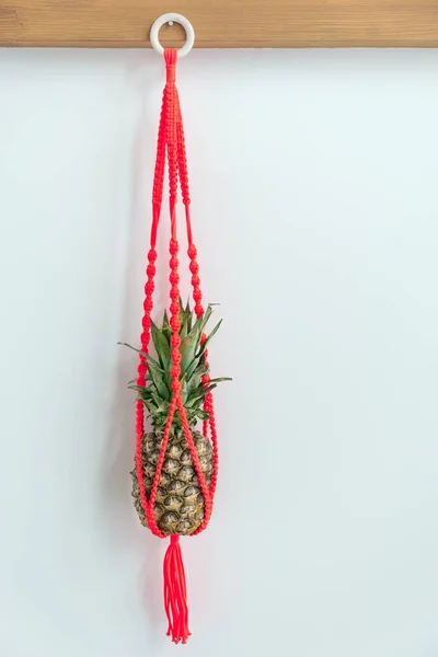 Piña fresca en macramé rojo colgando de un tronco de madera —  Fotos de Stock