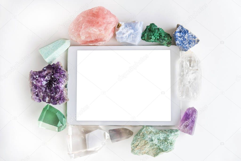 White touchpad with blank touchscreen framed by crystals and gemstones on a white background with blank space. Flat lay of frame with colorful gemstones and crystals