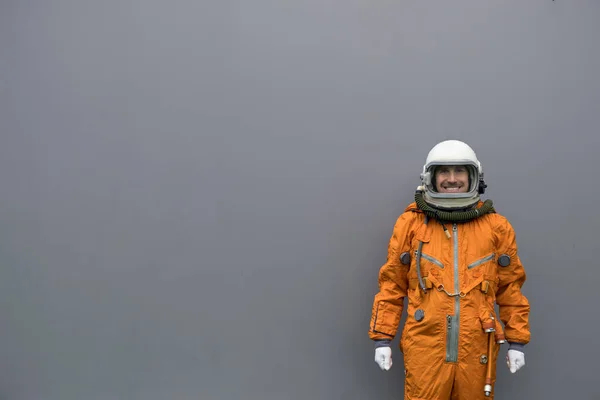 Astronaut in orangefarbenem Raumanzug und Helm vor grauem Hintergrund — Stockfoto