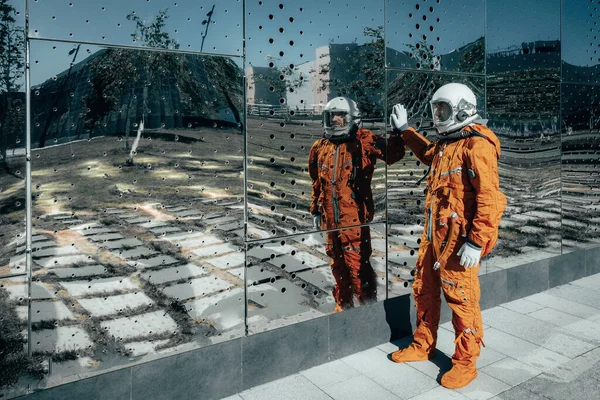 Astronaut in oranje ruimtepak en ruimtehelm bij een grote spiegelwand — Stockfoto