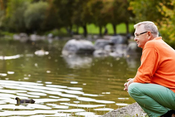 池の近くにしゃがんで中年の男性 — ストック写真