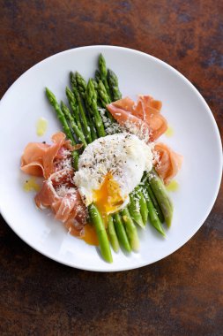 Parmesanlı Benedict usulü yumurta, yeşil kuşkonmaz ve Parma jambonu..