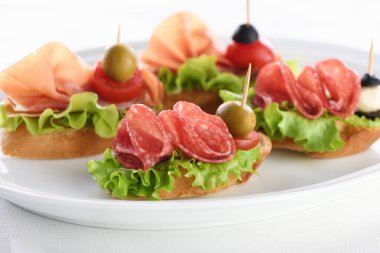 Yaprak salatalı, salamlı ya da Parma jambonlu, domatesli, mozzarella ve zeytinli yumuşak baget kanepeleri. Partide çeşitli tabaklar var..