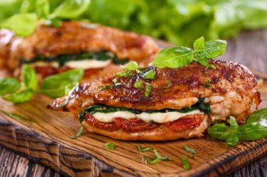 Fırında tavuk göğsü, mozarella, güneşte kurutulmuş domates, ıspanak. Et ahşap bir tahtada fesleğen ve marulla servis edilir..