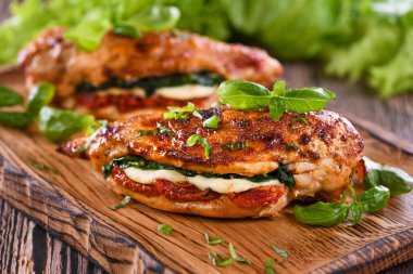 Fırında tavuk göğsü, mozarella, güneşte kurutulmuş domates, ıspanak. Et ahşap bir tahtada fesleğen ve marulla servis edilir..