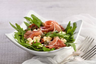 Arugula salatası, güneşte kurutulmuş domatesli jambon, mozzarella dilimleri, kapari zeytinyağı ve parmesanlı baharatlı. Sağlığını gözetleyenler için bir yemek.