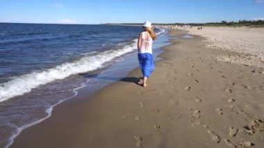 Genç bir kadın sahilde yürüyor.