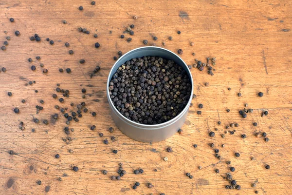 Pimienta negra dentro del frasco y en la mesa de madera — Foto de Stock