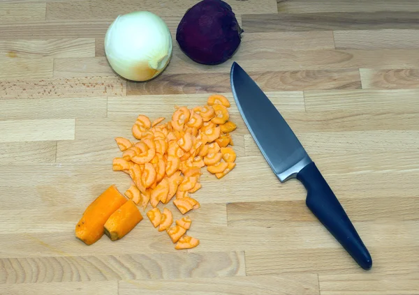 Zanahorias en rodajas y un gran cuchillo de cocina de acero con mango negro acostado sobre tabla de cortar marrón. Vista de cerca —  Fotos de Stock