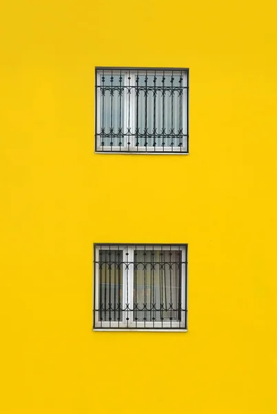 Mur de bâtiment jaune avec deux fenêtres avec grille métallique — Photo