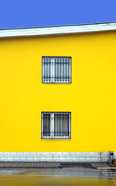 Mur de bâtiment jaune avec deux fenêtres avec grilles métalliques — Photo